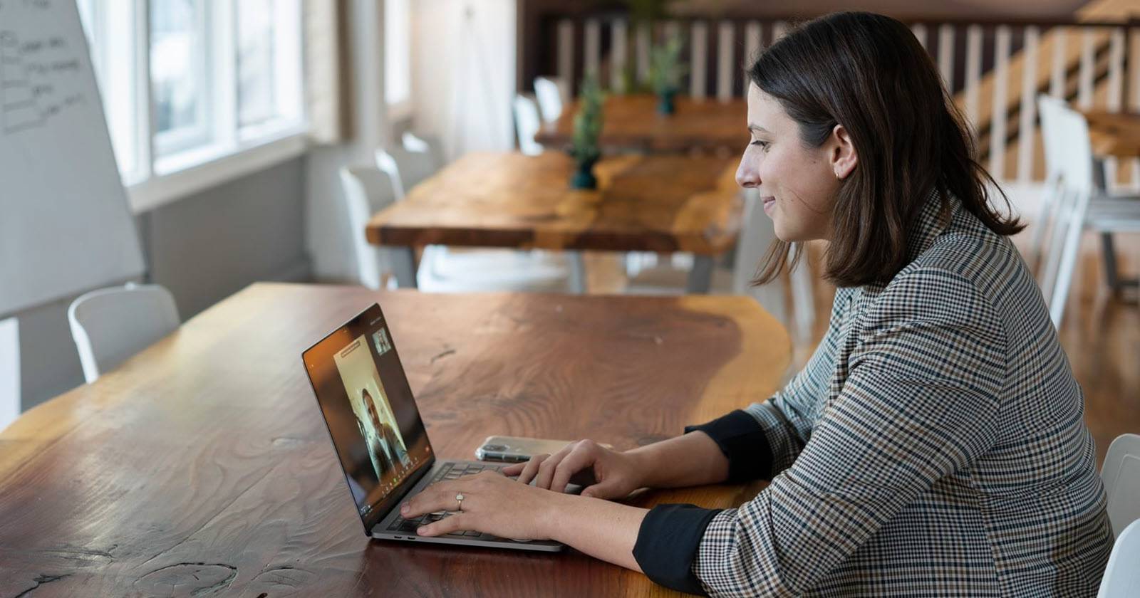женщина на виртуальной встрече, смотрит в камеру и использует ноутбук