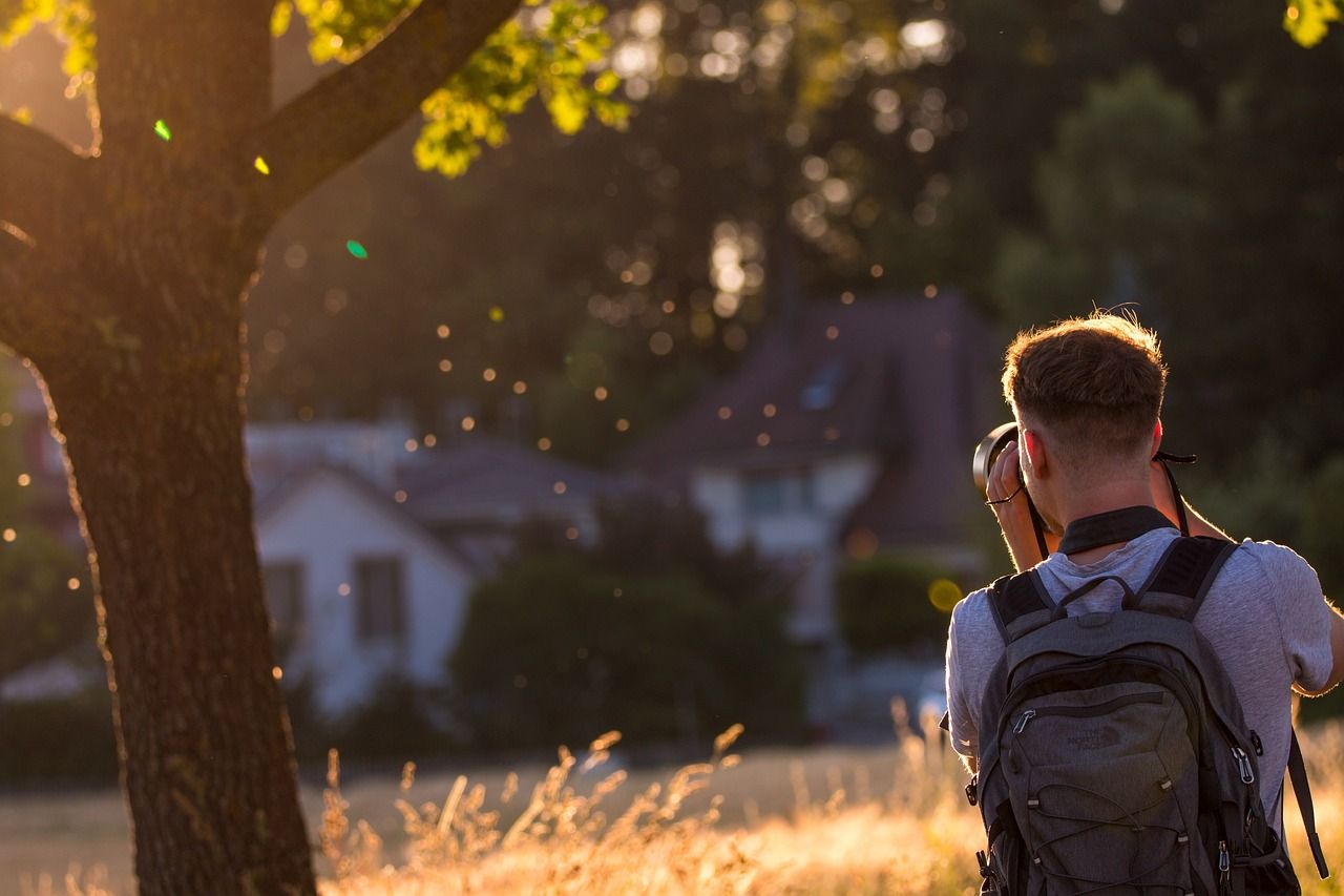 Съёмка через плечо: человек фотографирует дом на золотом часе