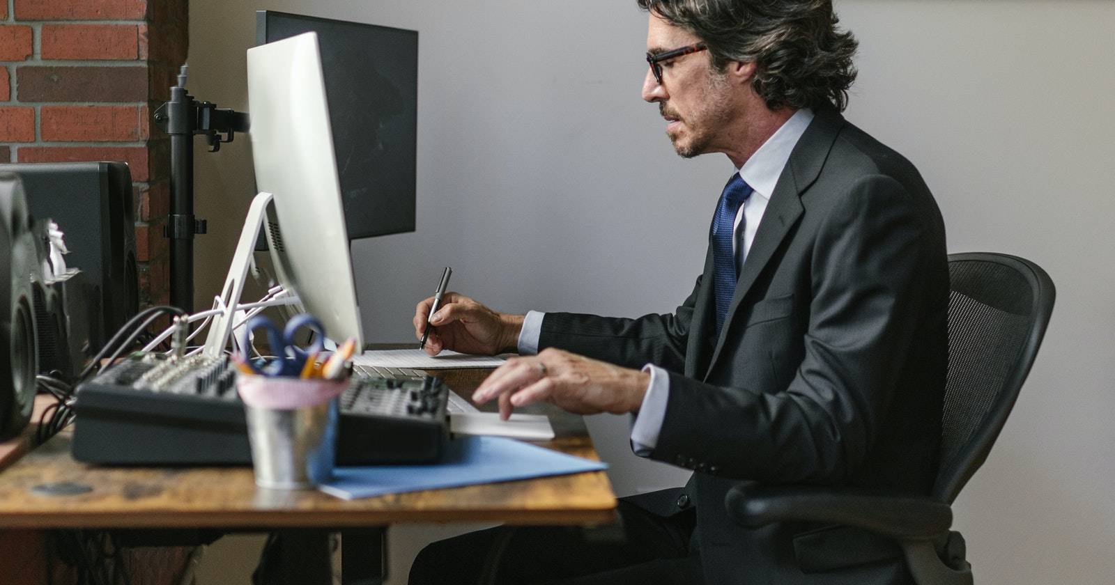 Мужчина в костюме работает за столом, ноутбук и документы вокруг