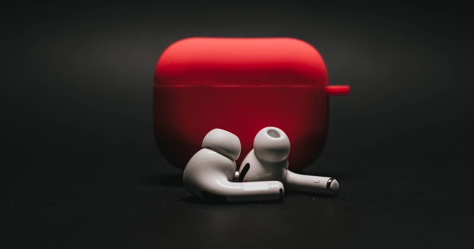 Белые AirPods с красным футляром на чёрном фоне