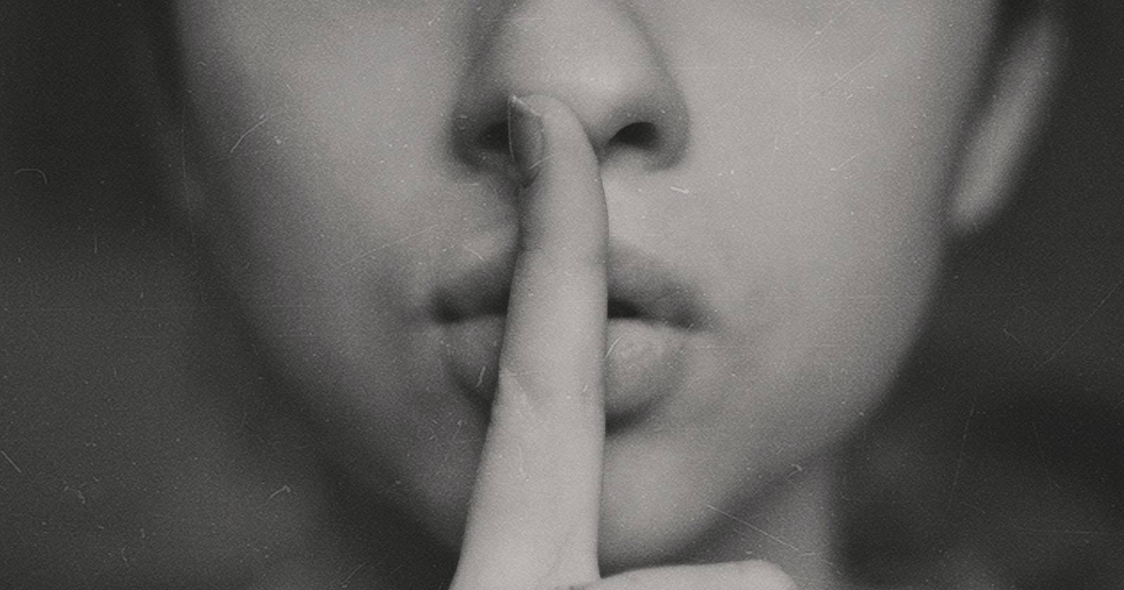 Фотография человека, прикладывающего указательный палец к губам в жесте «тишина»