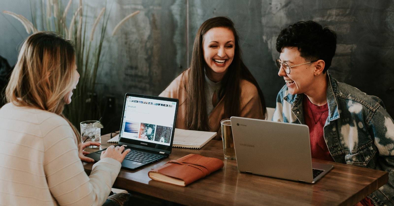 Three laughing teenagers sitting around a table with their laptops