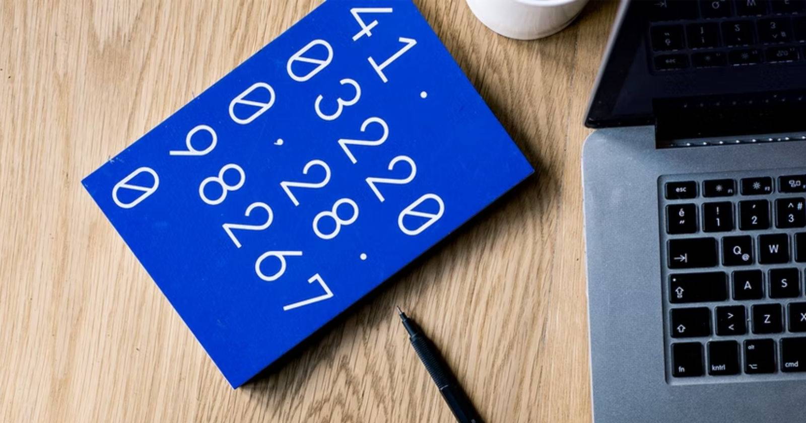 Синий блокнот с цифрами на обложке рядом с ноутбуком и ручкой на деревянной поверхности