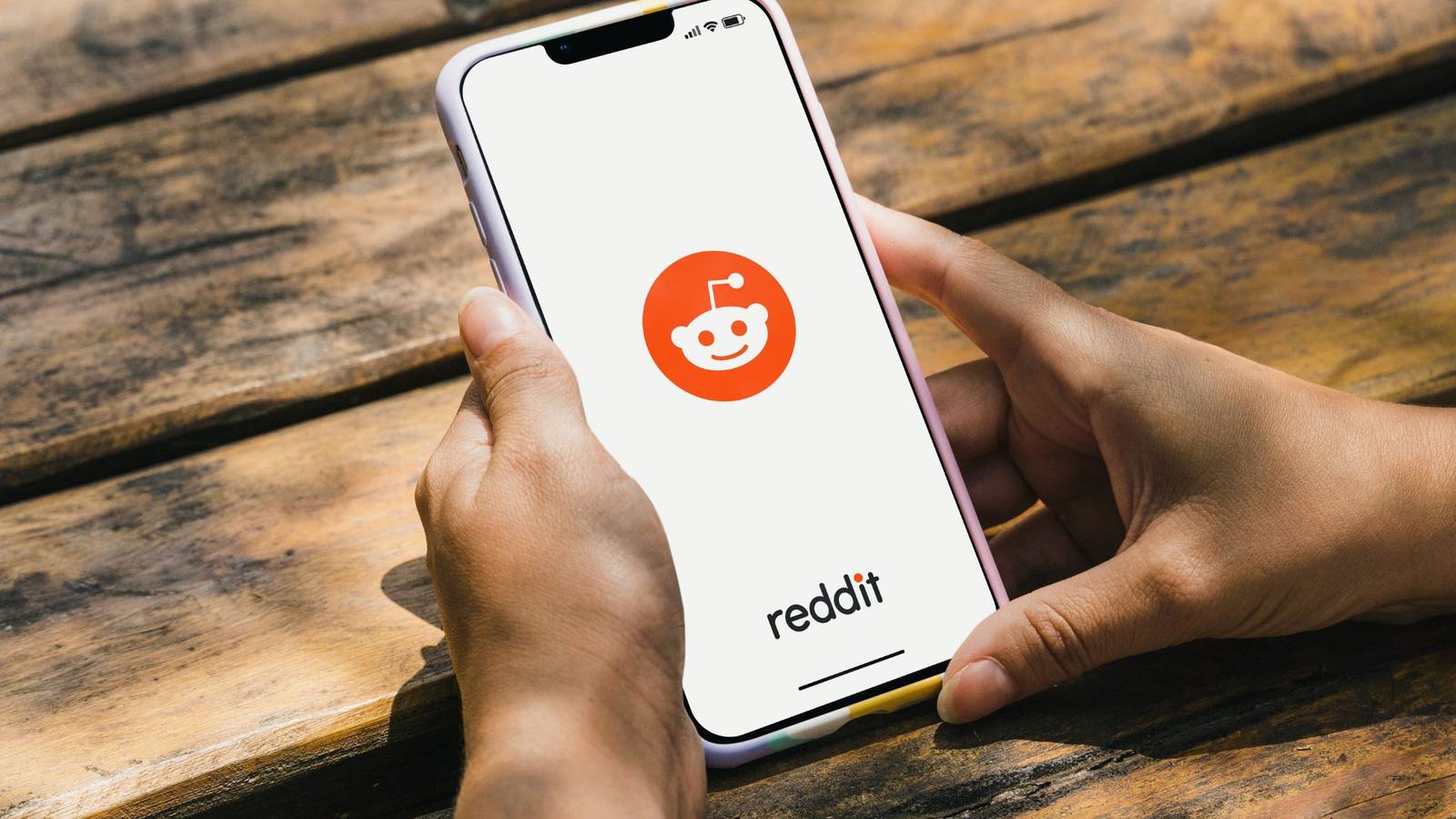 смартфон с логотипом Reddit в руках на столе