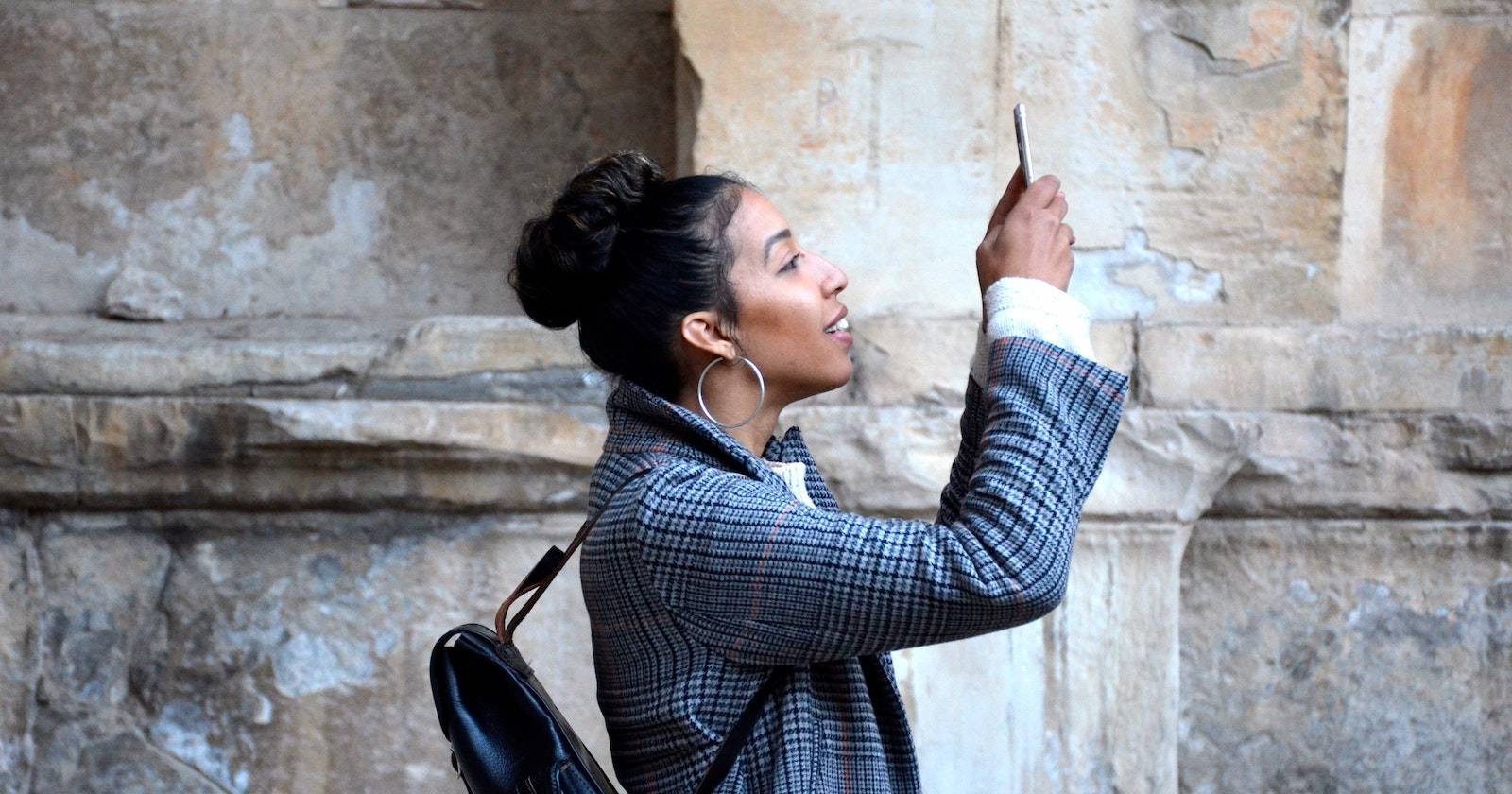 Женщина делает фото на телефон, поза фронтальная, уличное окружение