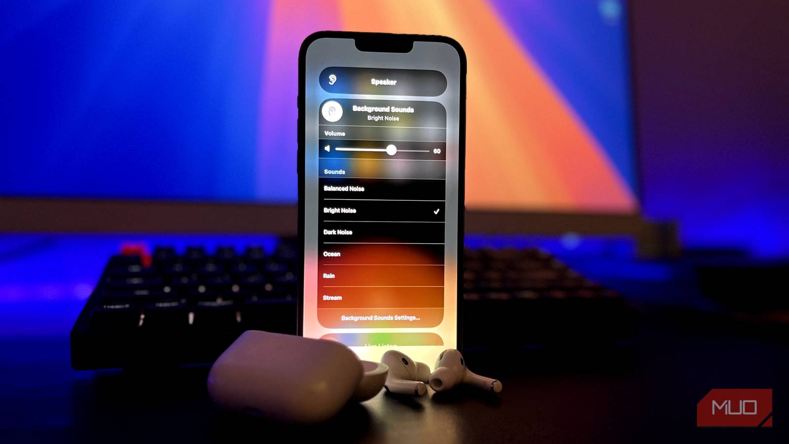 iPhone воспроизводит фоновые звуки с AirPods Pro на переднем плане, монитор и клавиатура на заднем плане.