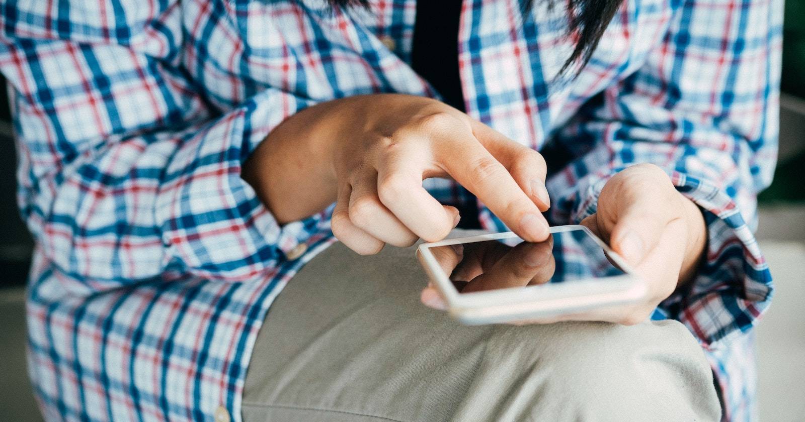 Человек сидит и печатает сообщение на iPhone; видны только руки и одно колено