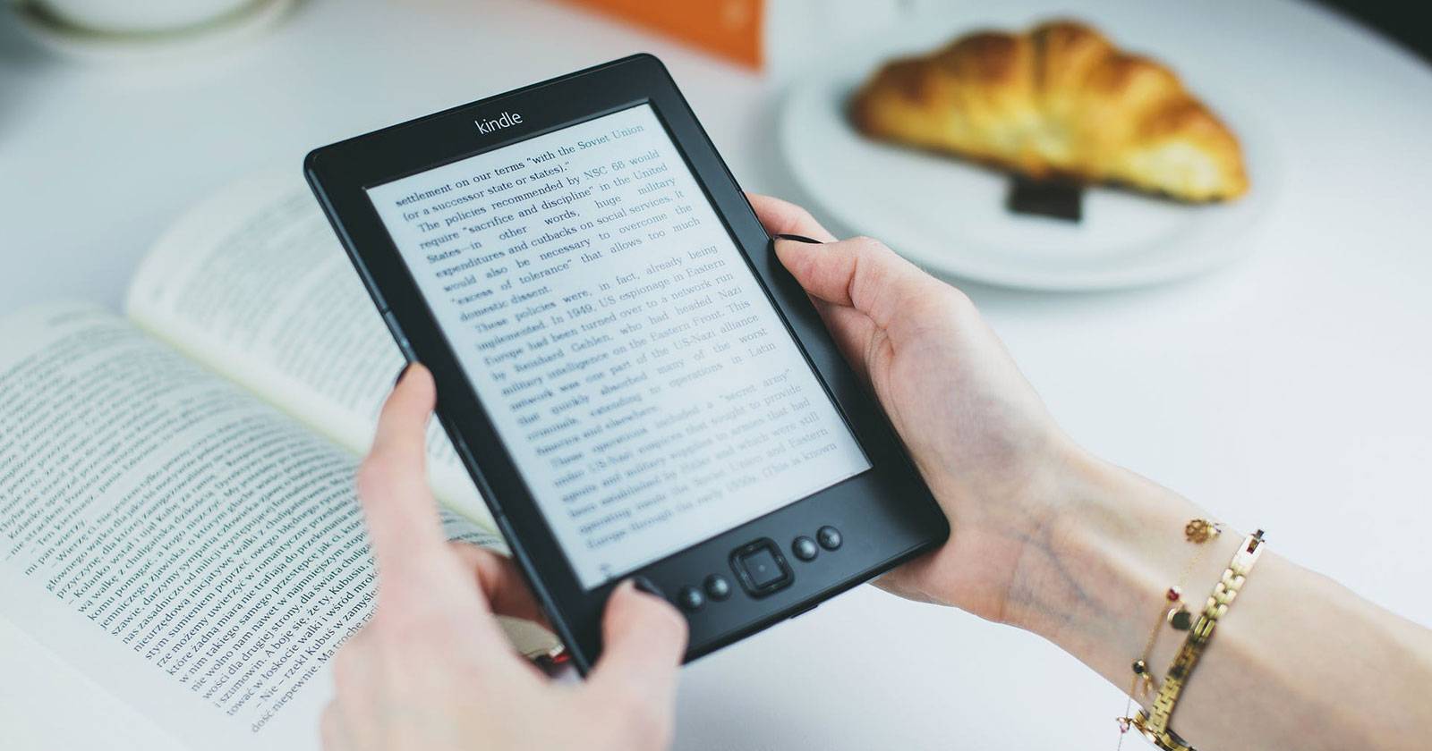 Руки держат старую модель Kindle и читают книгу