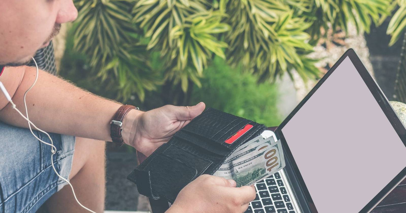 Мужчина достаёт деньги из кошелька рядом с подержанным ноутбуком