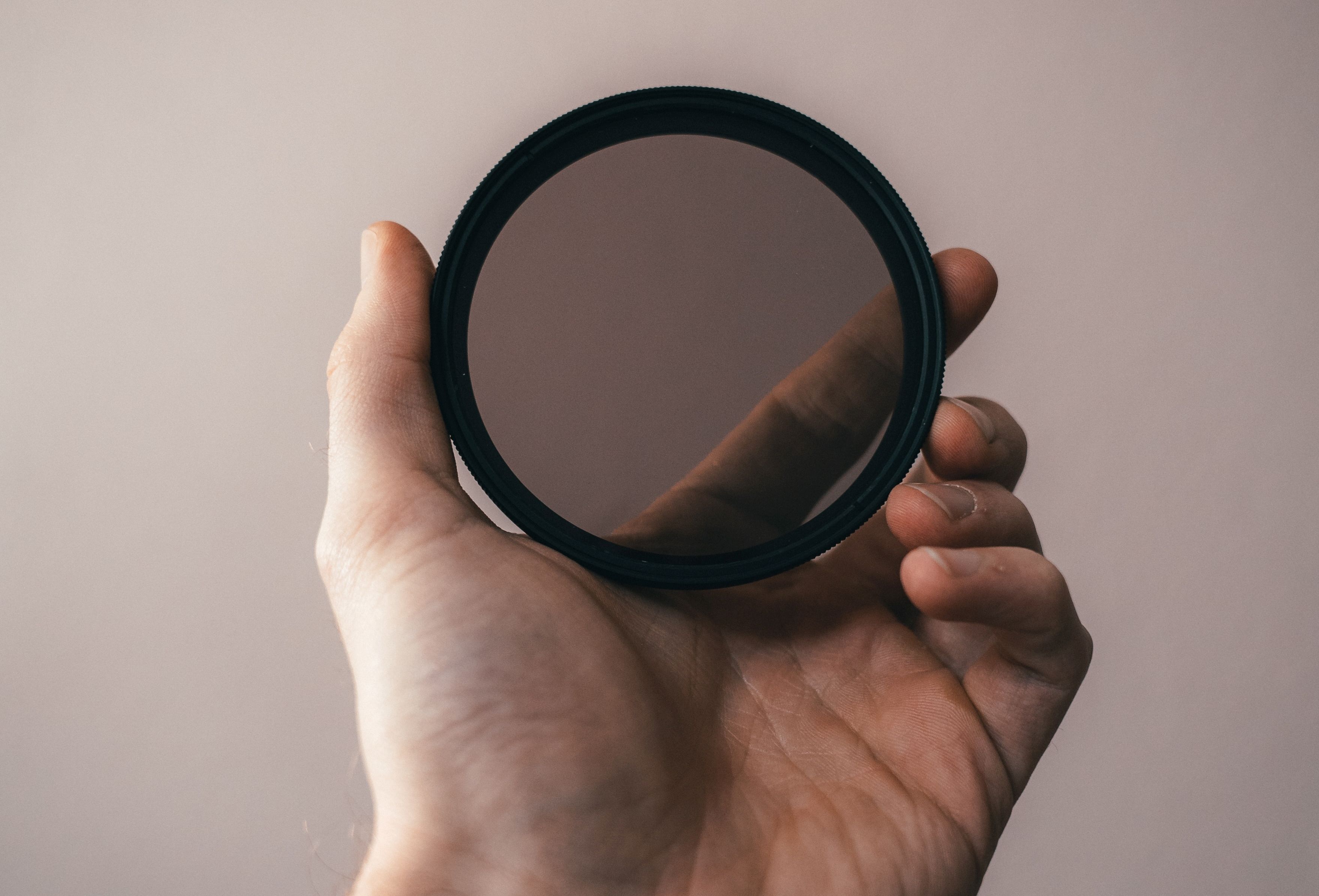 Человек держит в руках защитный фильтр для объектива.