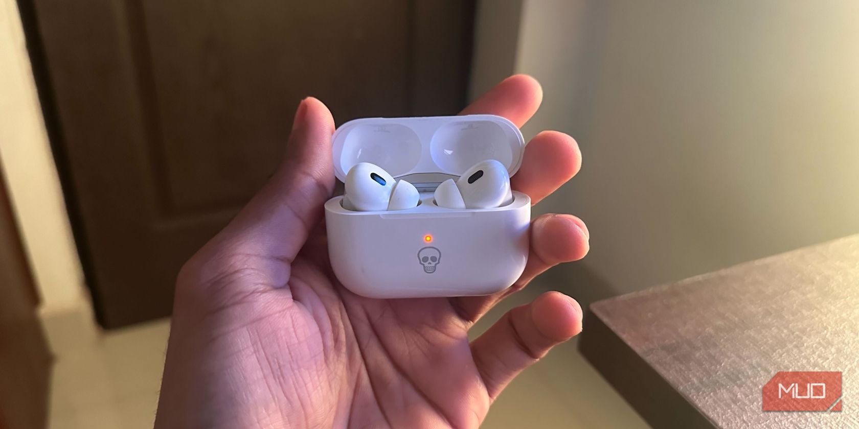 Человек держит наушники AirPods Pro в зарядном кейсе с оранжевым индикатором
