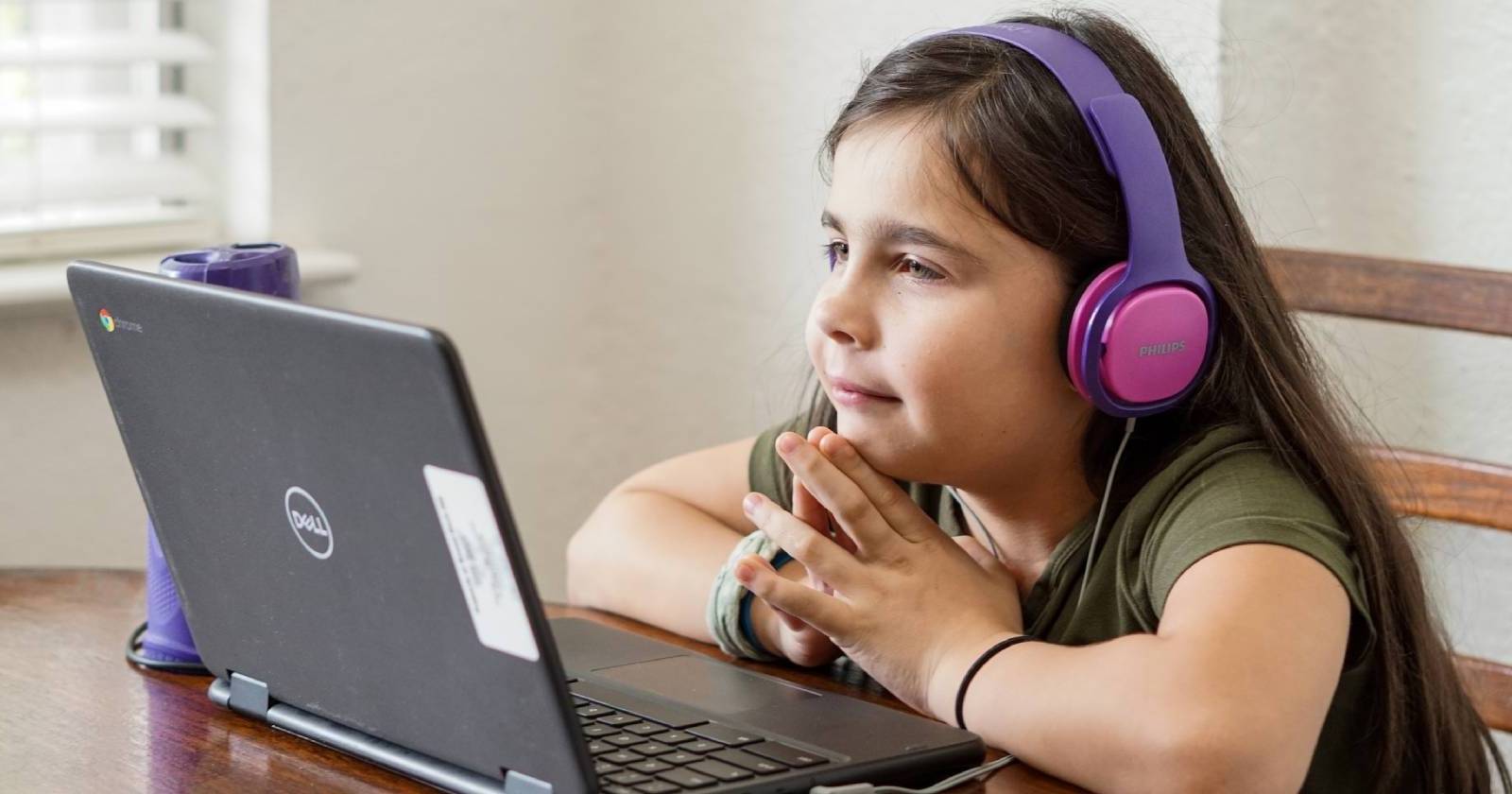 Ребёнок в наушниках смотрит на ноутбук и занимается онлайн