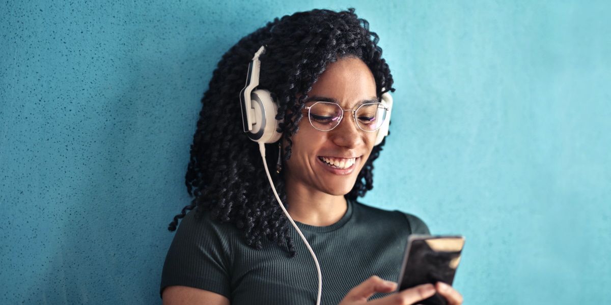 smiling woman with glasses listening to audio on her phone using a white headset