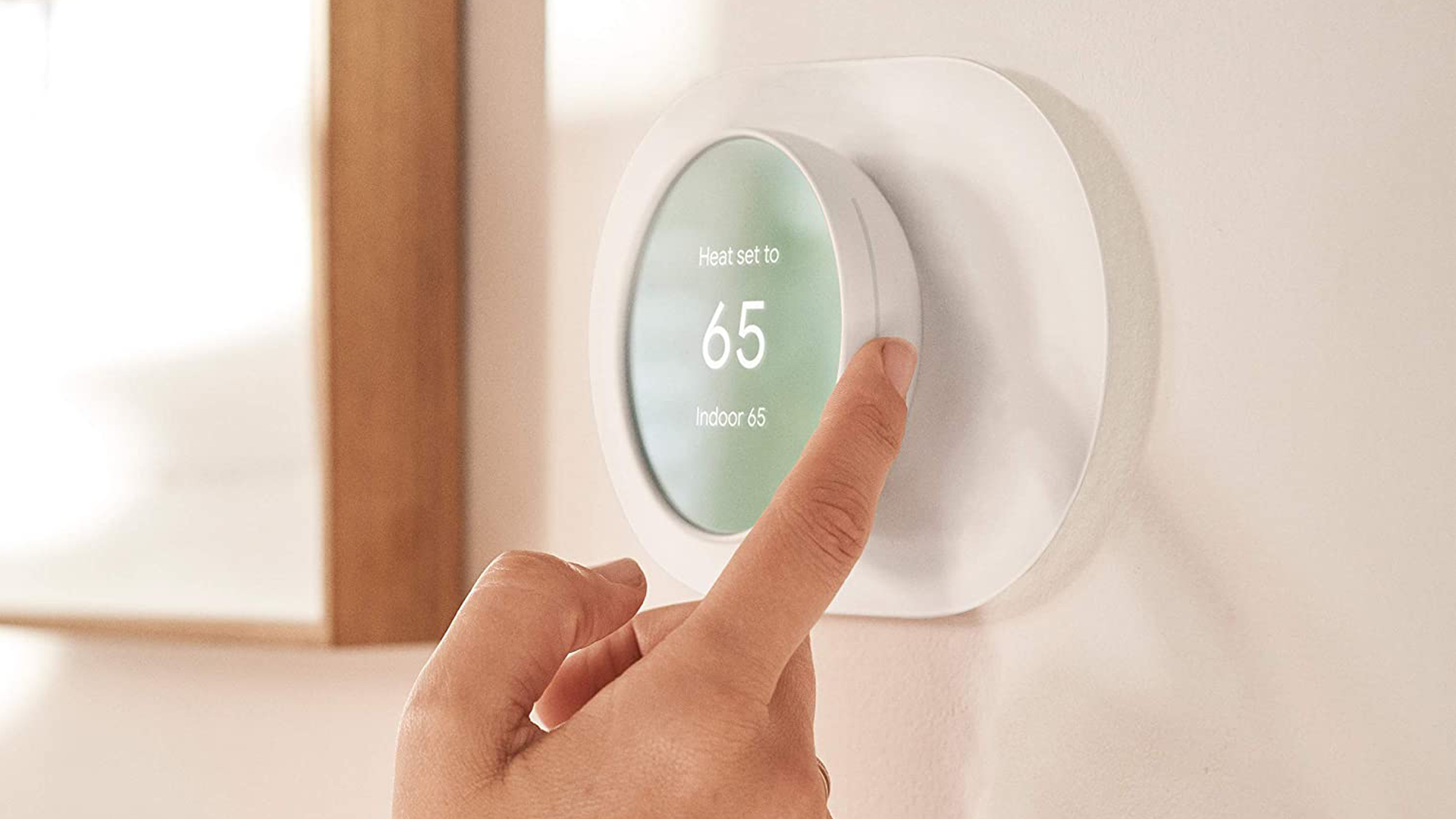 A person adusting a Google Nest Smart Thermostat with their finger.