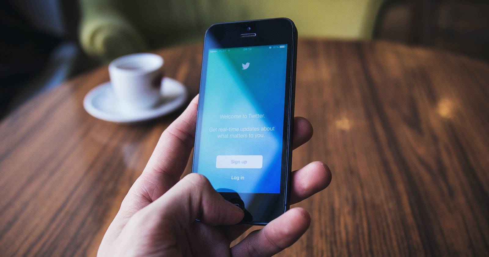 Рука держит мобильный телефон с экраном приветствия Twitter