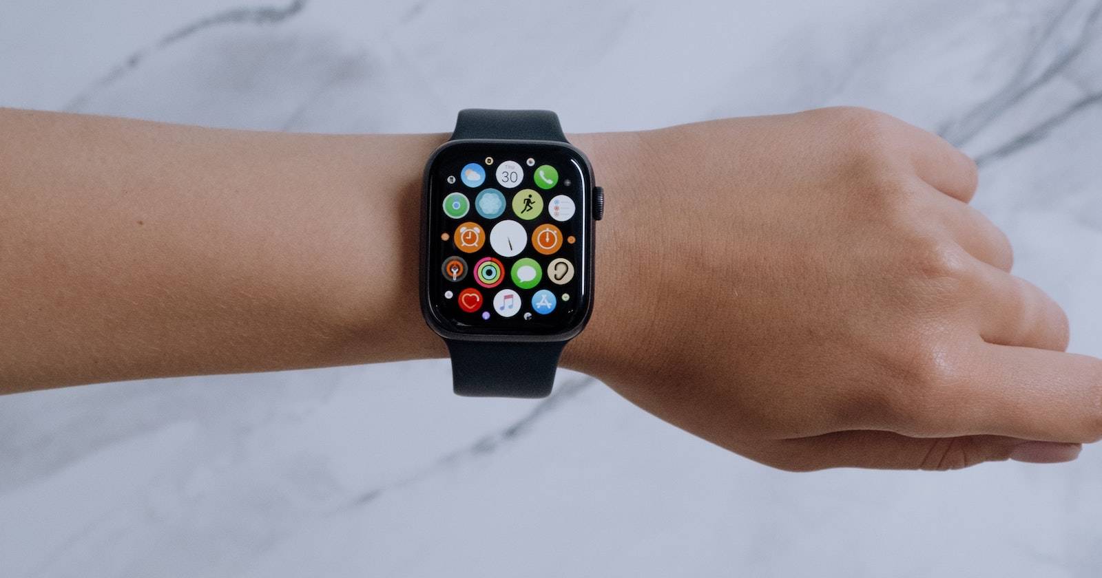 Рука в сжатом кулаке с Apple Watch на запястье; видны все приложения на экране