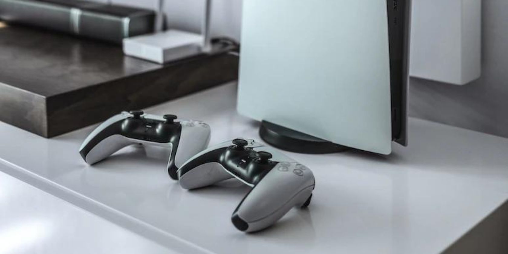 Два контроллера DualSense рядом с PS5 на чёрно‑белой фотографии