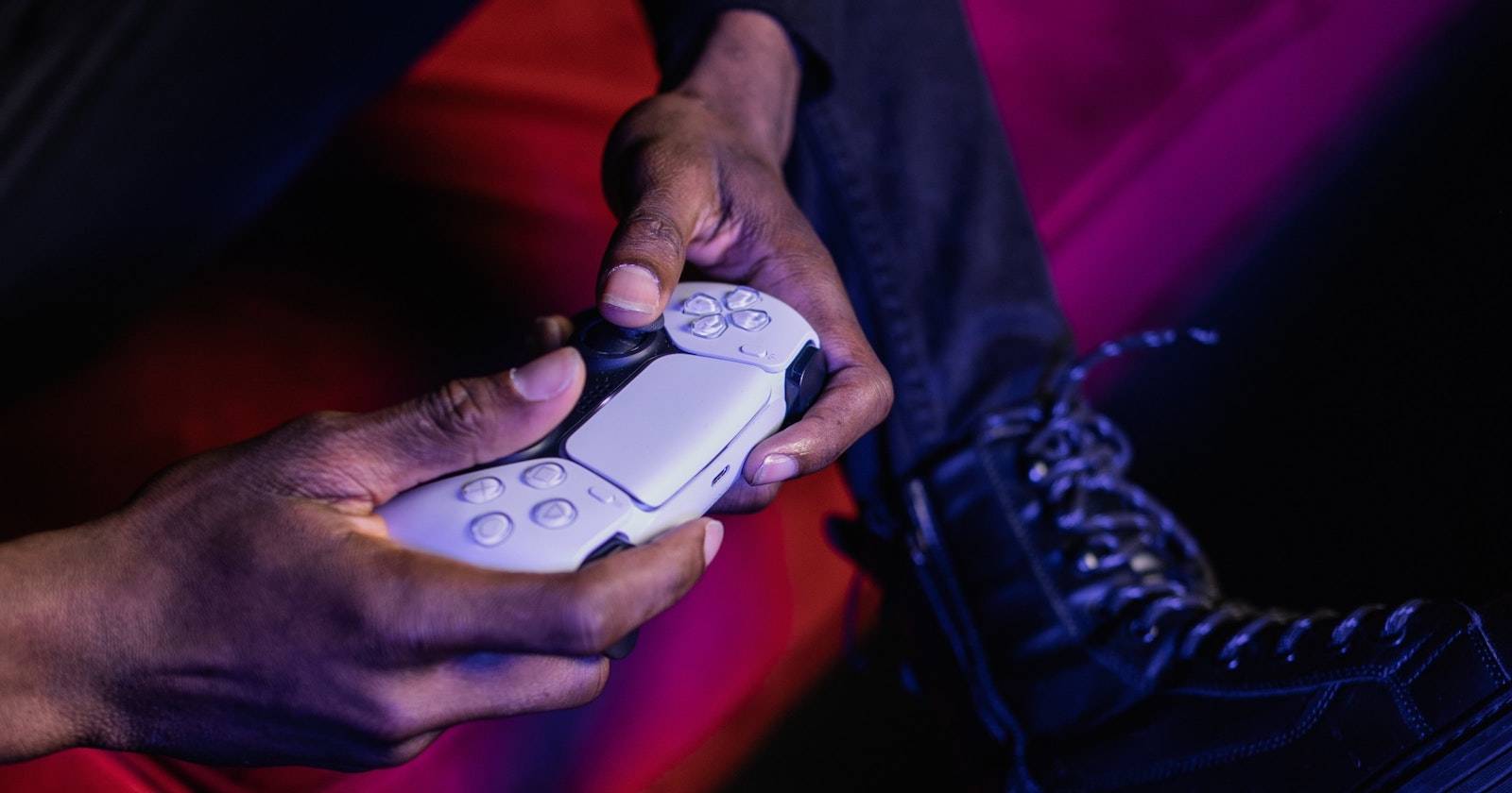 Человек в чёрных ботинках держит контроллер DualSense