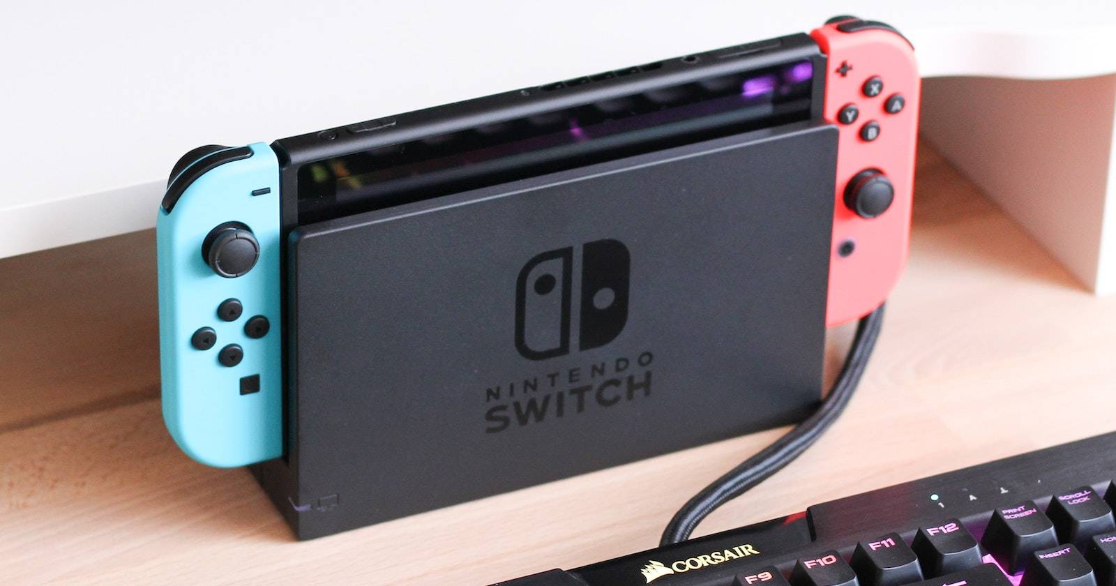 A Nintendo Switch in a dock, behind a computer keyboard
