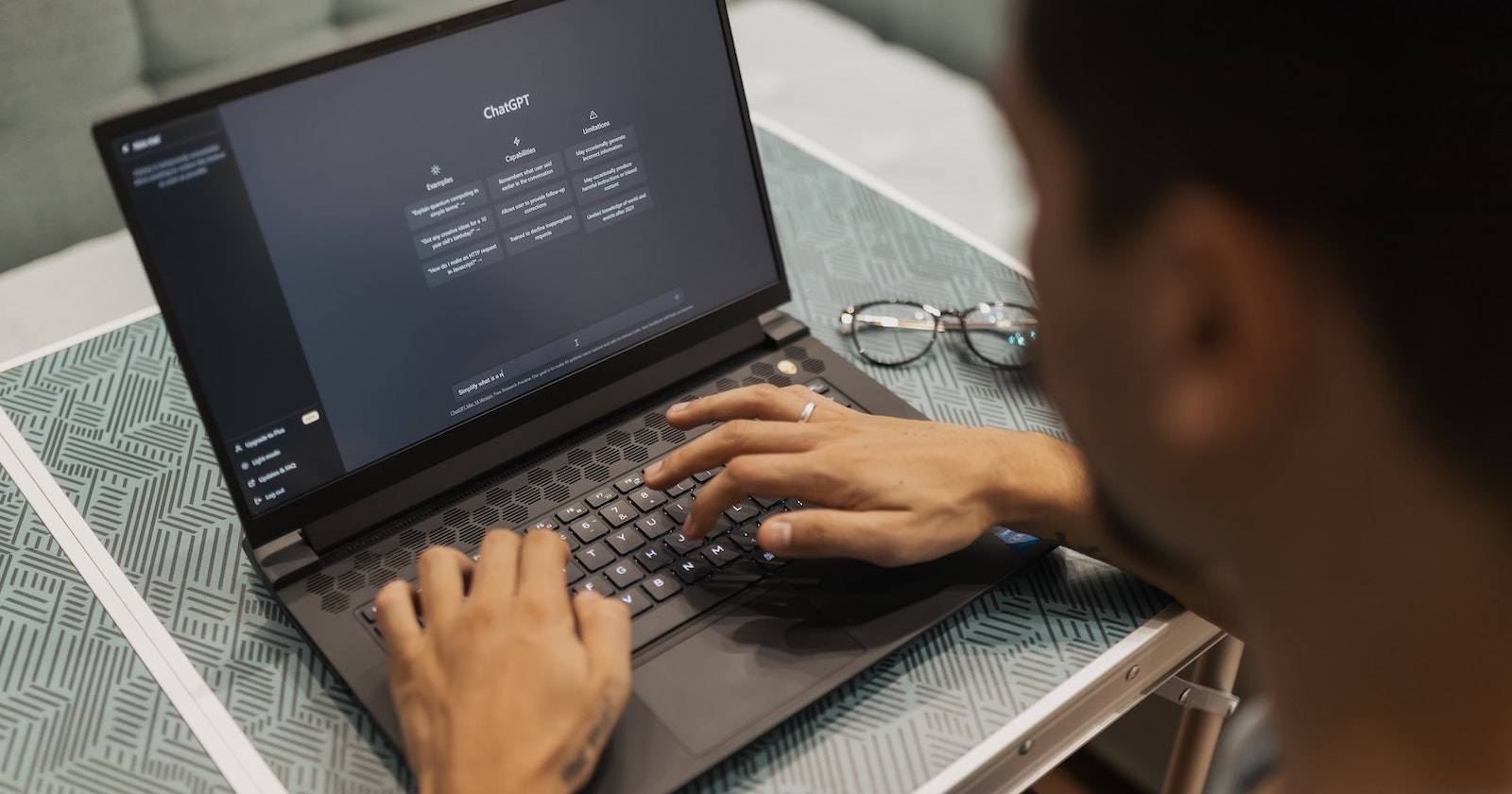 Человек использует ChatGPT в тёмной теме на ноутбуке, очки рядом