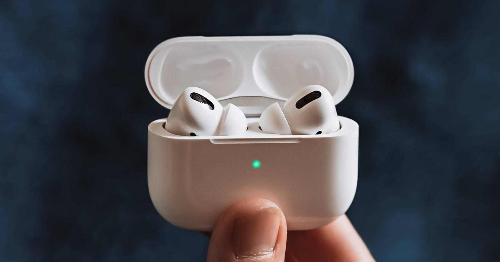 AirPods Pro being charged while being held in the hand, with the indicator light shining green.