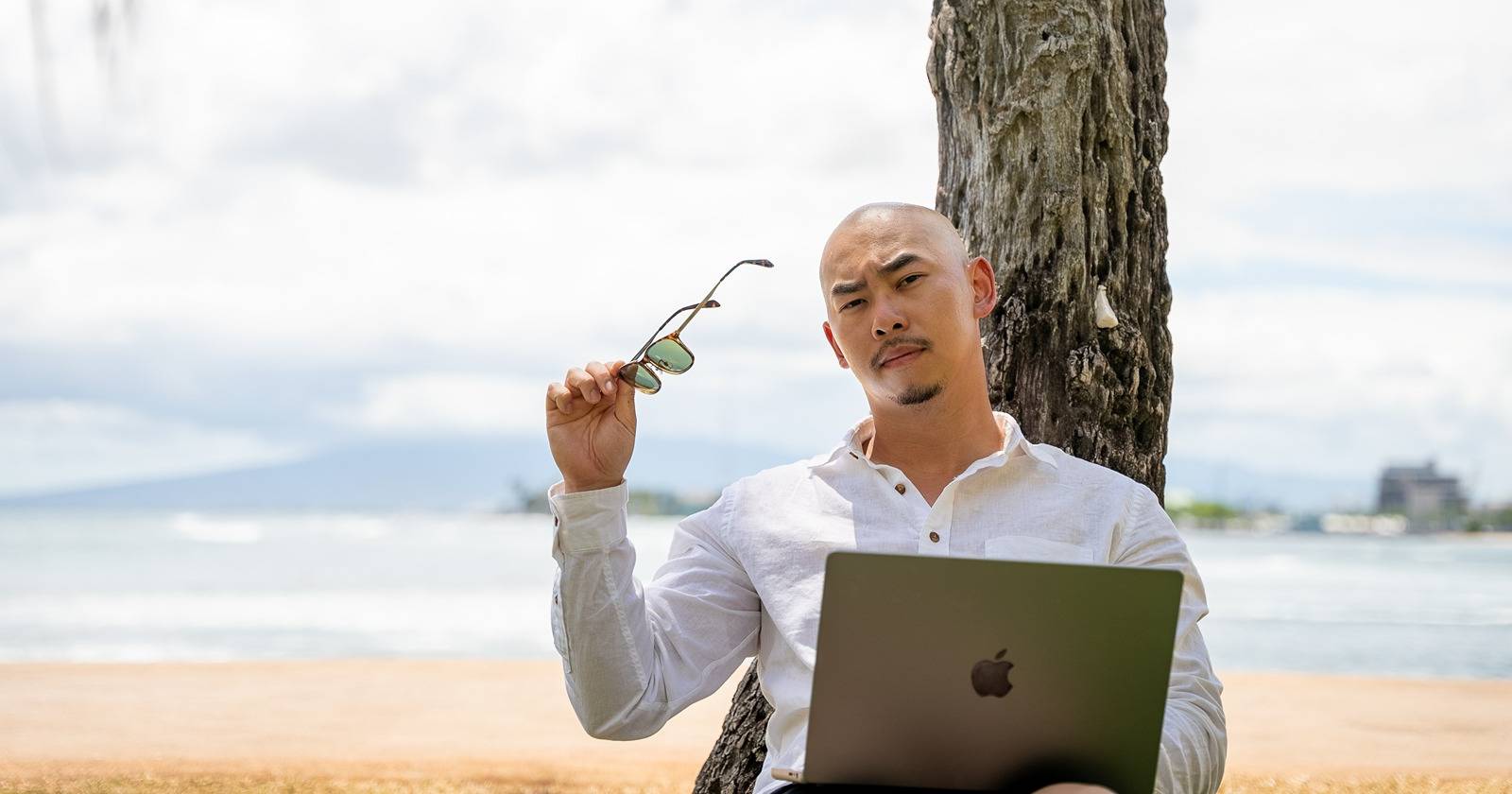 мужчина на пляже держит солнцезащитные очки в руке