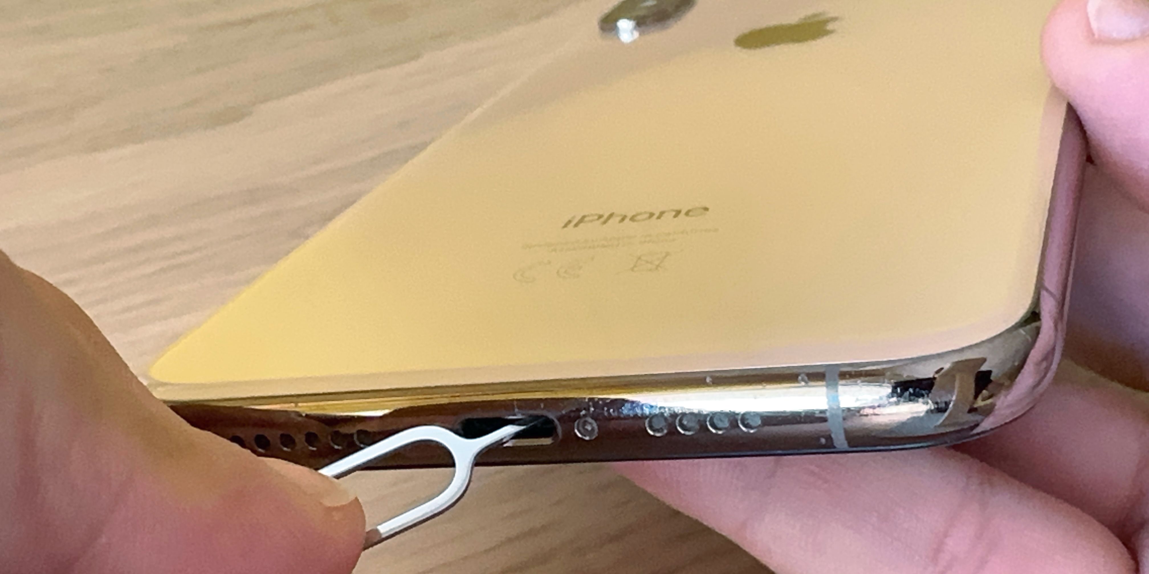 iPhone XS Max в руке, инструмент для извлечения SIM вставлен в Lightning-порт