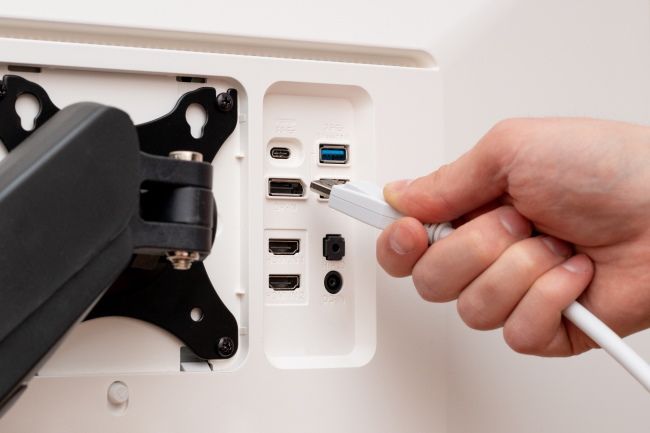 A hand plugging a display cable into the back of a monitor.