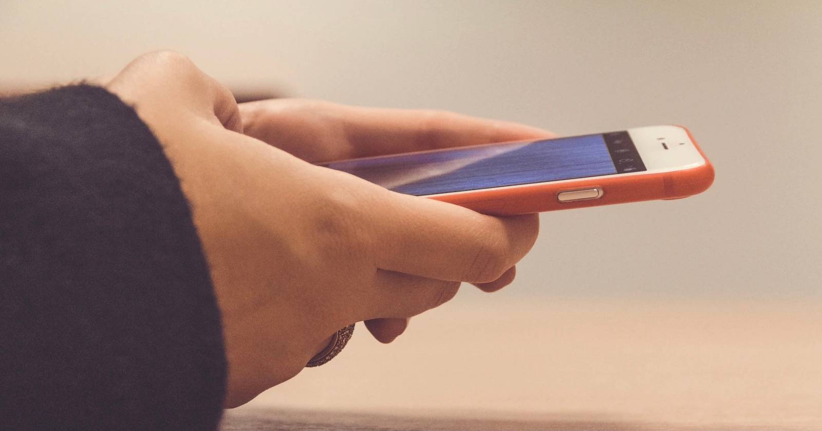 Руки держат iPhone в оранжевом чехле, демонстрируя процесс съёмки экрана.