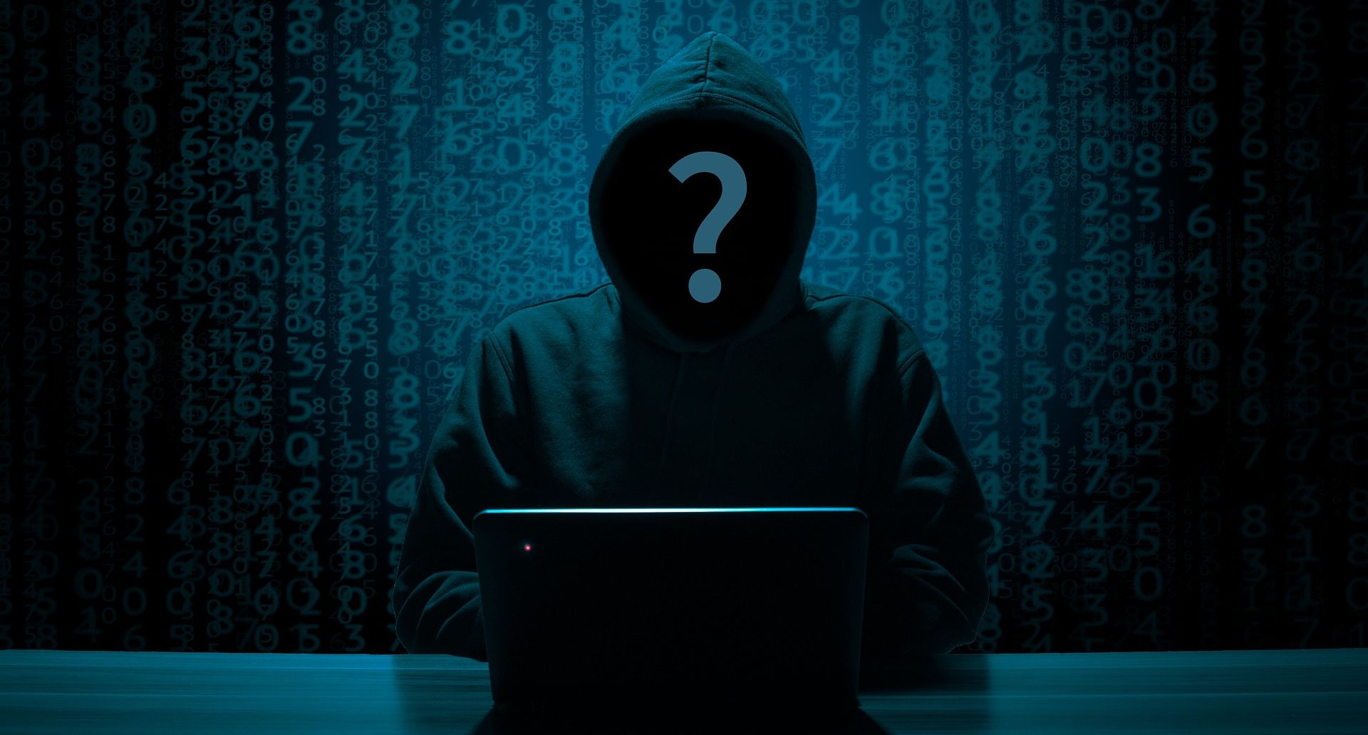 anonymous hooded individual using laptop in dark room