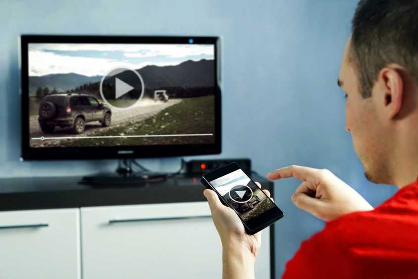 Мужчина смотрит видео на смарт‑ТВ с сопутствующим приложением на смартфоне