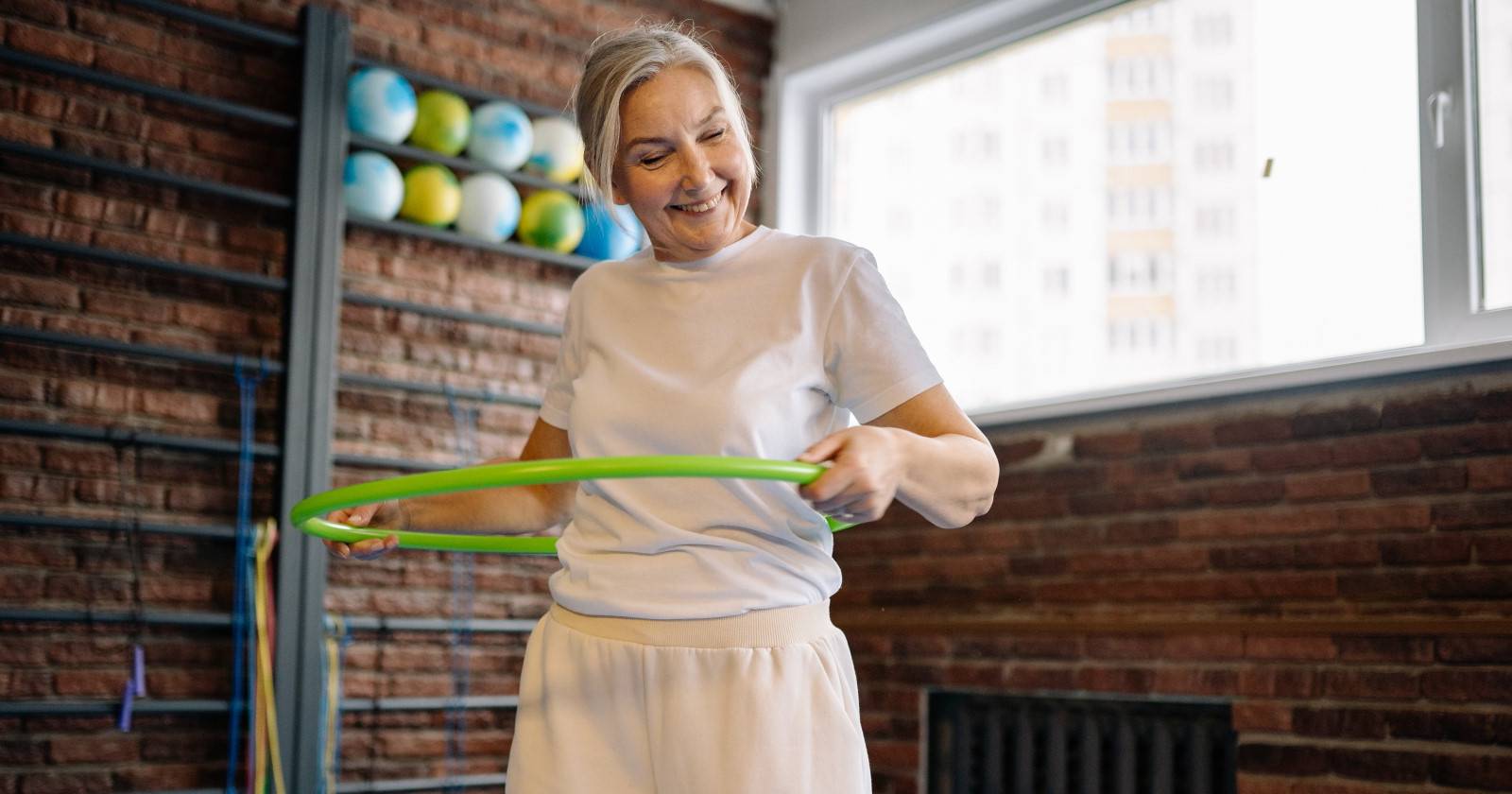 Пожилая женщина улыбается и использует зелёный хула-хуп