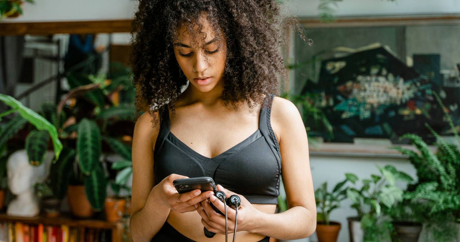 женщина в спортивной форме смотрит на iPhone и держит скакалку