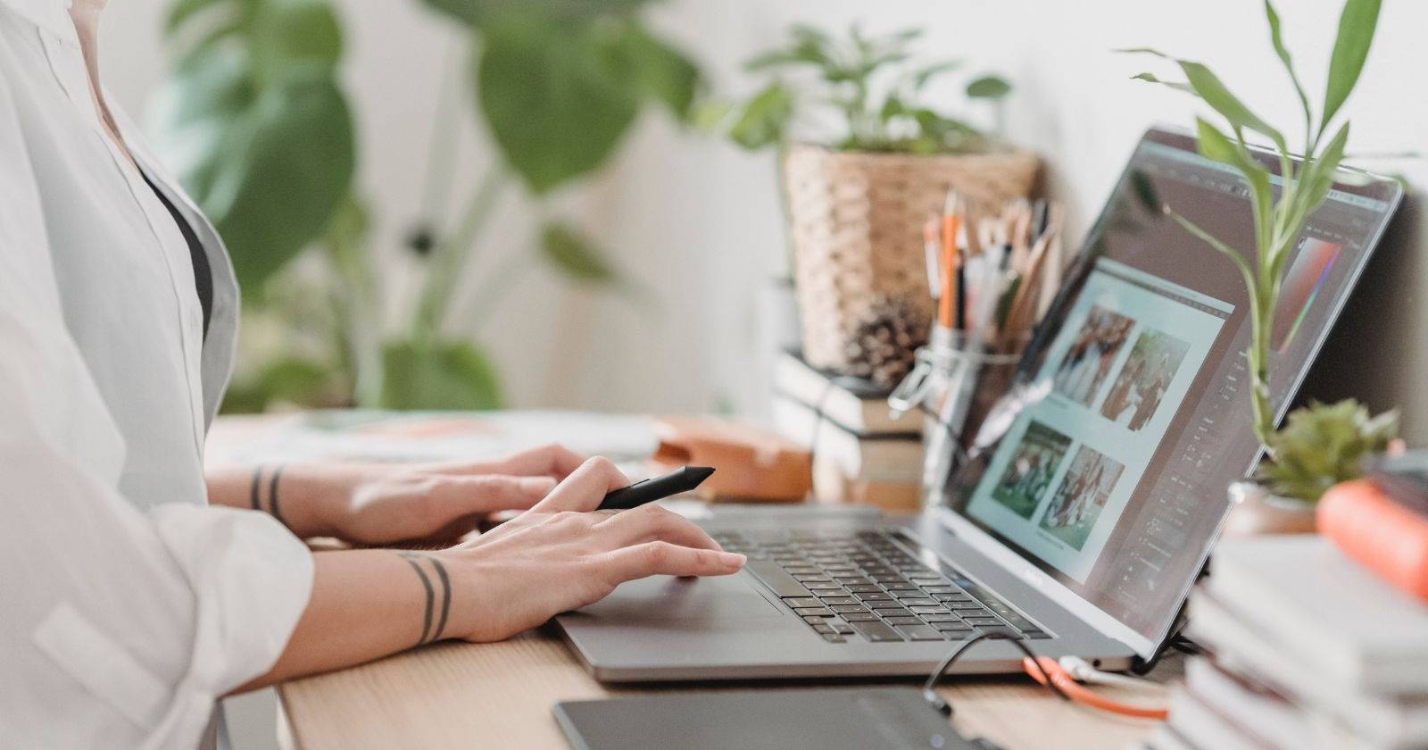 Женщина держит стилус и печатает на ноутбуке — вид сбоку