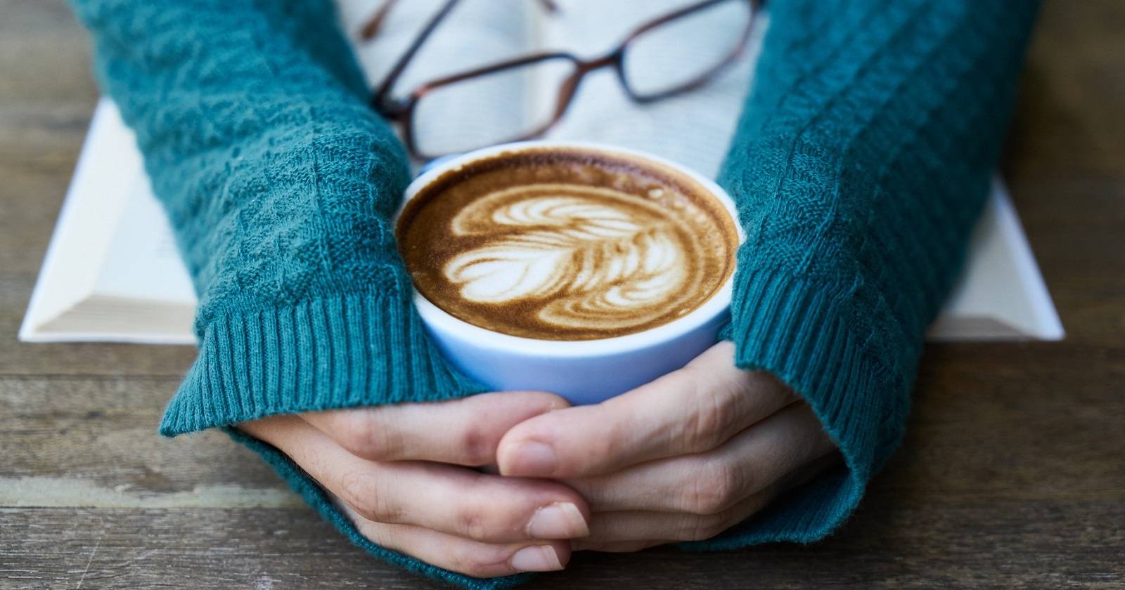 Человек держит чашку кофе над блокнотом