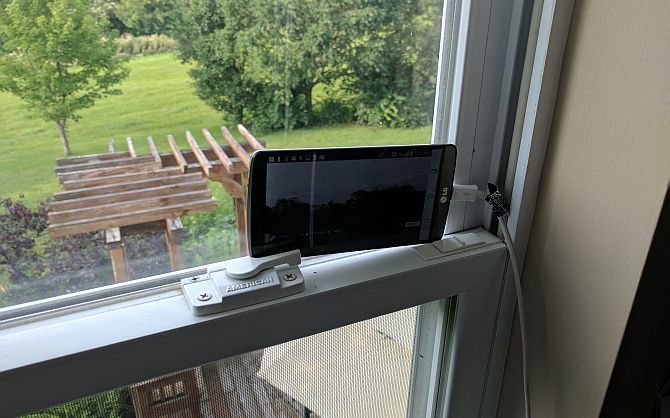 Телефон, установленный на подоконнике, снимающий двор через окно