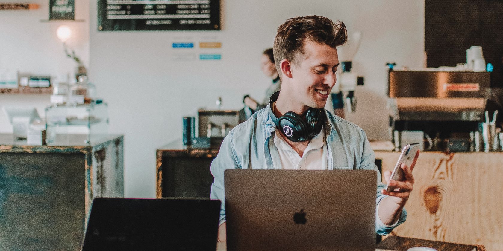 Мужчина улыбается, работая за компьютером и глядя на телефон