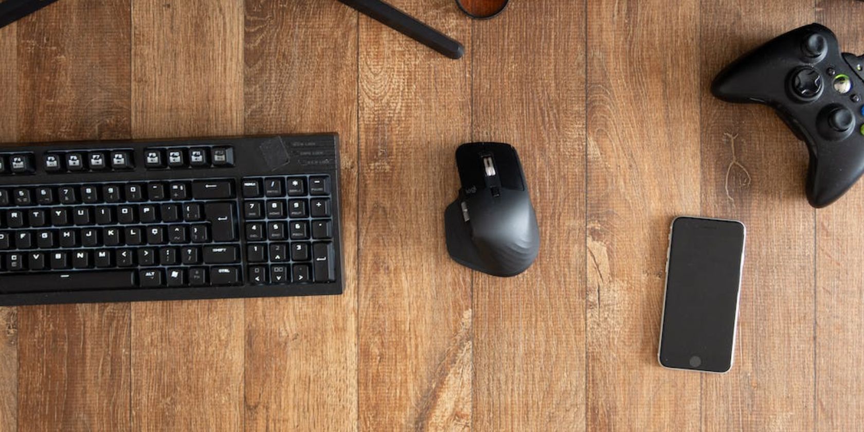 Mouse keyboard iphone and xbox controller on wooden desk