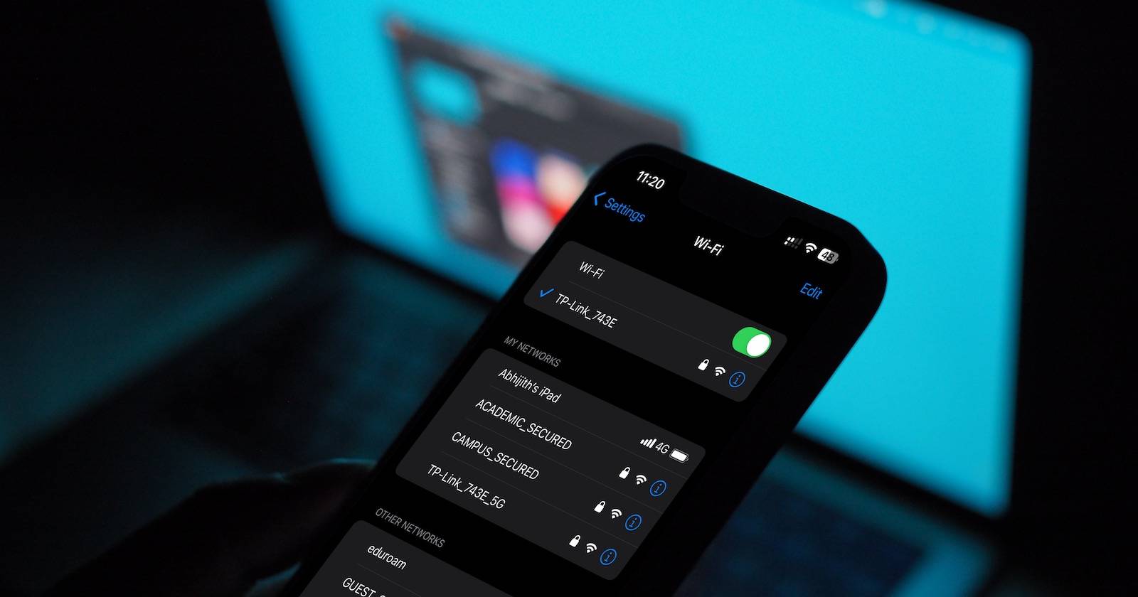 Меню Wi‑Fi на iPhone, на заднем плане MacBook