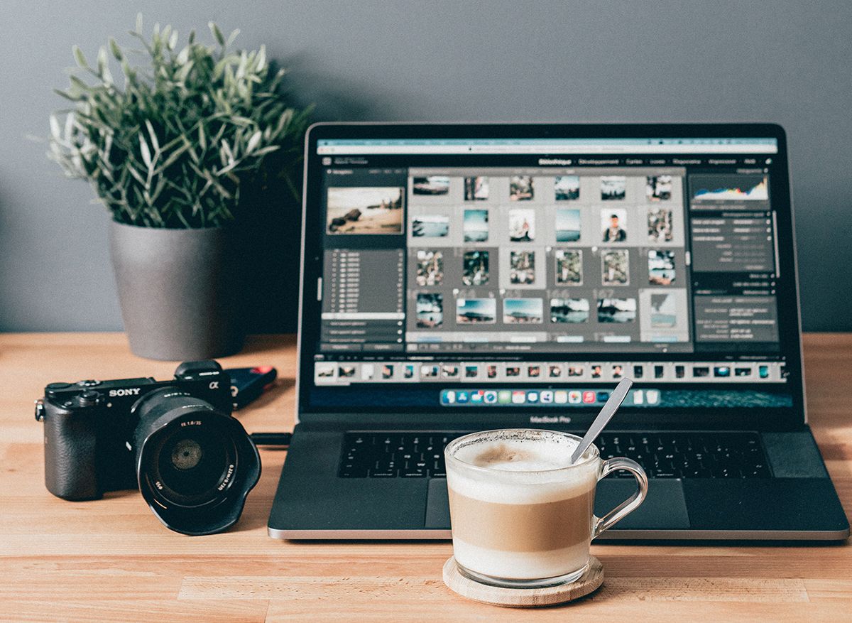 Ноутбук с открытым Lightroom, камера, кофе и растение на столе