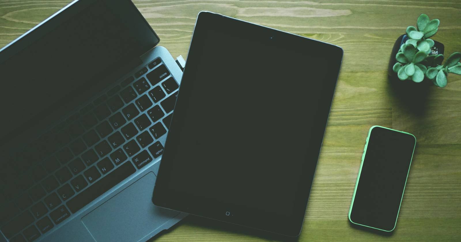 MacBook рядом с iPhone и iPad на столе.