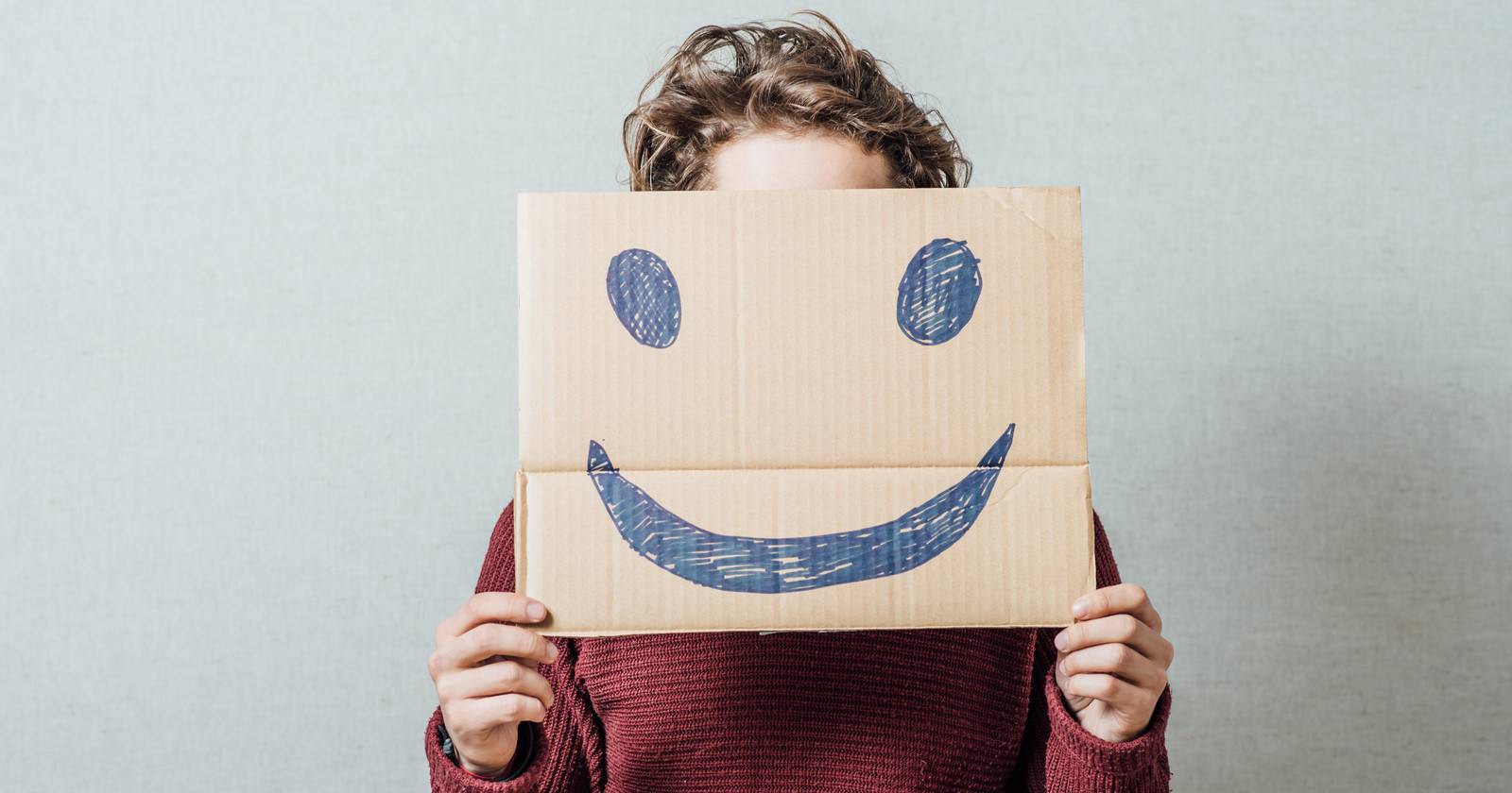 Человек держит картонную улыбку перед лицом