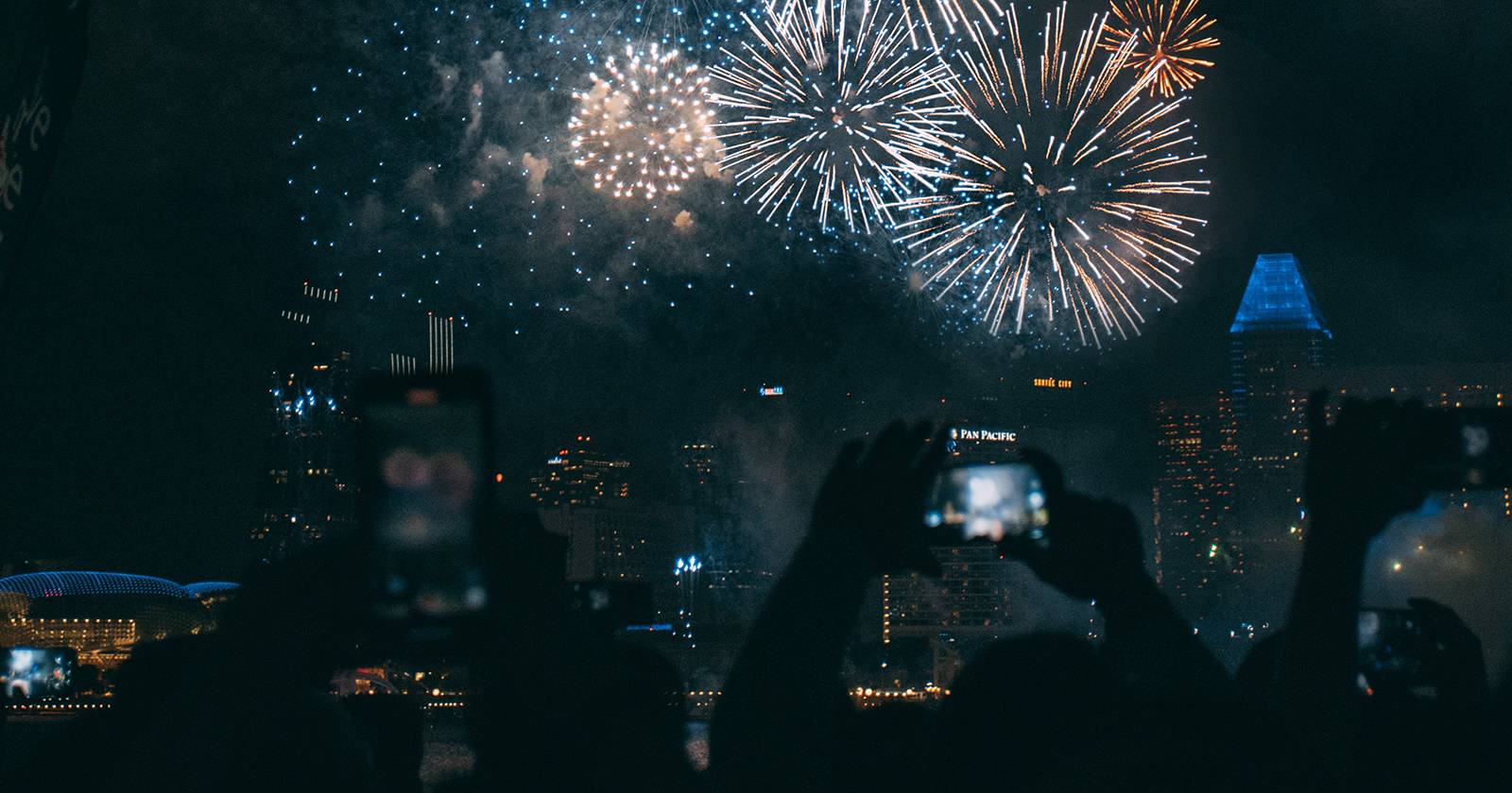 Группа людей, снимающих фейерверки на смартфоны.